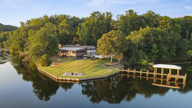 The house among the trees above the lawn, the seawall and the covered pier, reflected in the creek