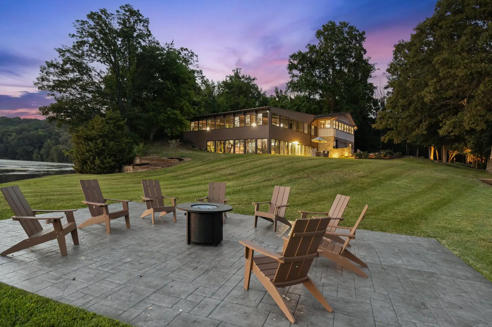 Adirondack chairs around the fire pit at dusk, with the house lit up behind