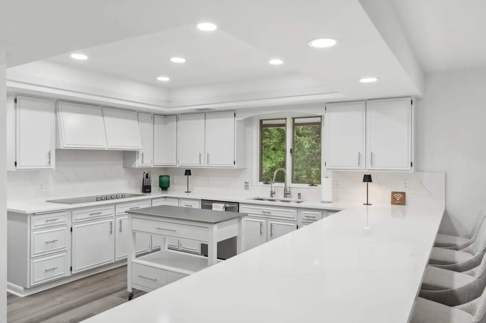 The white kitchen with a large island, wall ovens and windows onto the trees