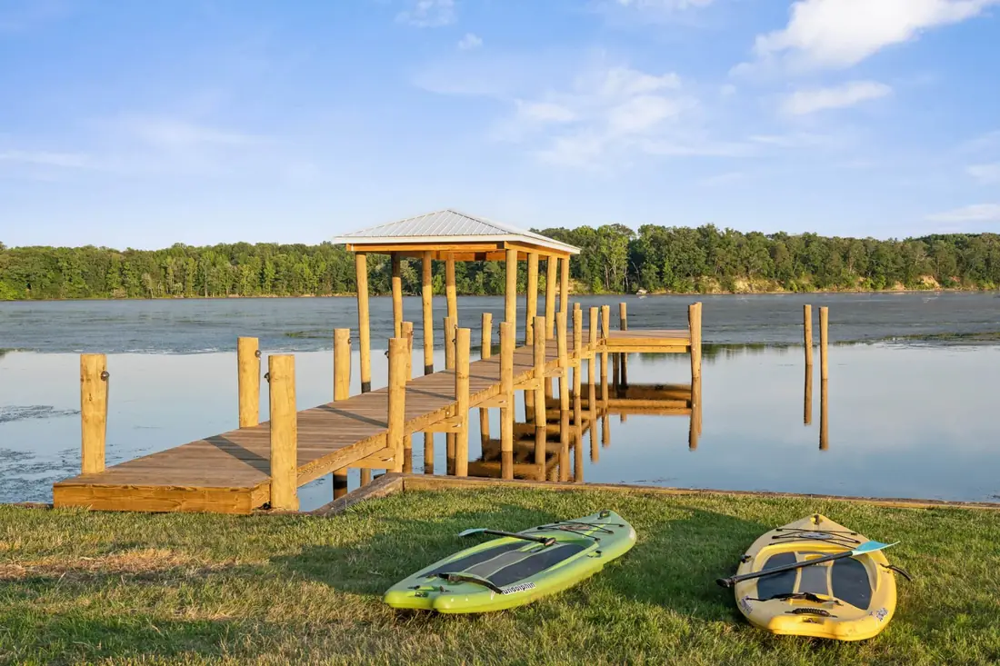 The covered pier on the creek with paddleboards and kayaks on the grass