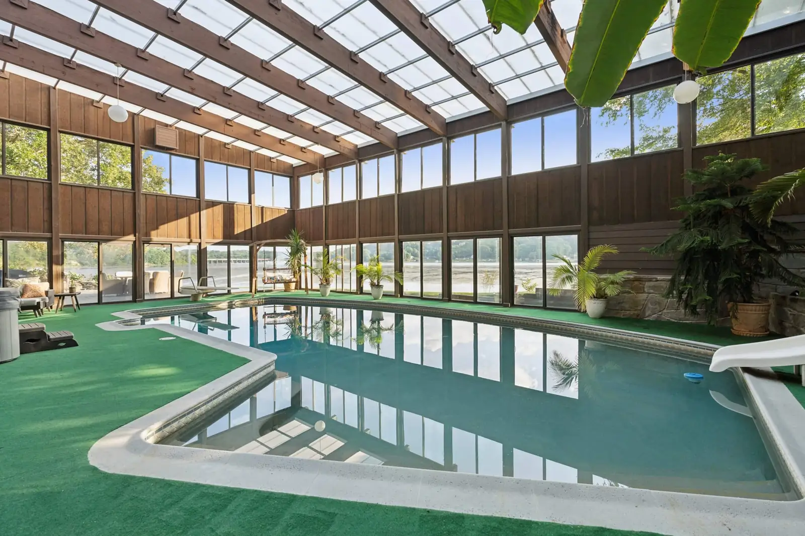 The long indoor pool under a timber-framed roof, lined with plants and a stone wall